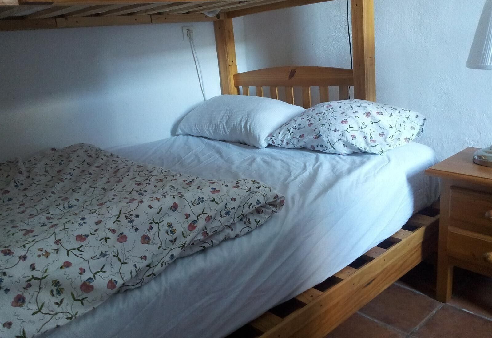Un lit simple avec un cadre en bois, une literie blanche et des oreillers à motifs floraux.