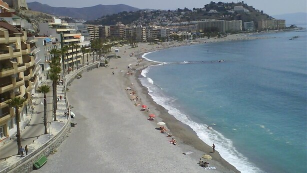 A coastal cityscape with a wide beach, buildings along the shore, and a mountain in the background.