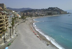 A coastal cityscape with a wide beach, buildings along the shore, and a mountain in the background.