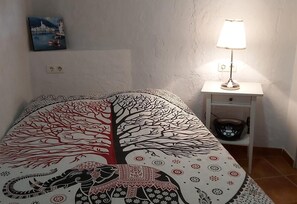 Un lit orné d’un motif représentant un arbre et un éléphant, une table de chevet avec une lampe et un tableau accroché au mur.