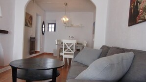 A living room with a sofa, a round table, and a dining area with chairs and a chandelier.