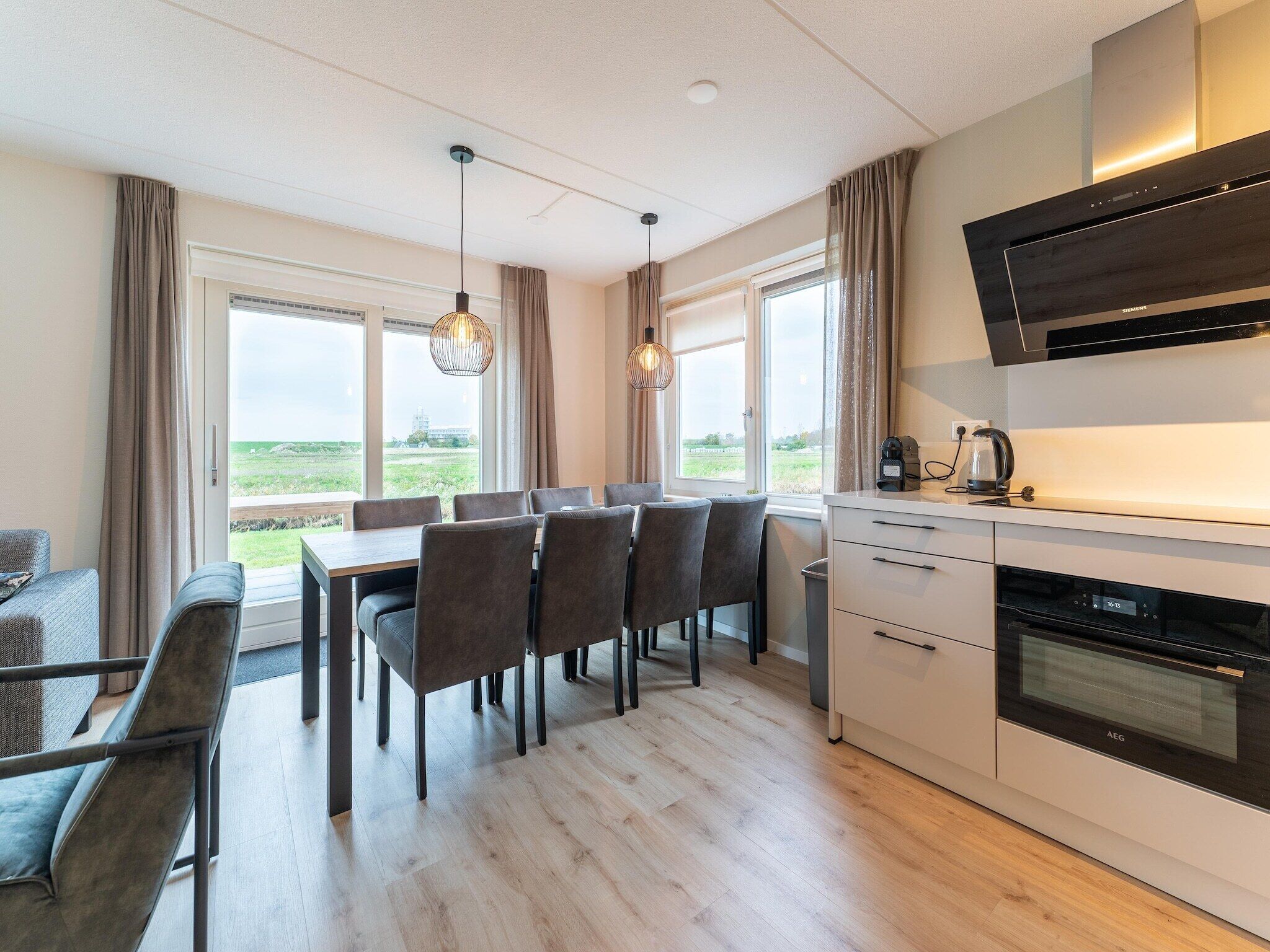 A modern kitchen with a built-in oven, a dining area with a table and chairs, and large windows offering a view of the outdoors.