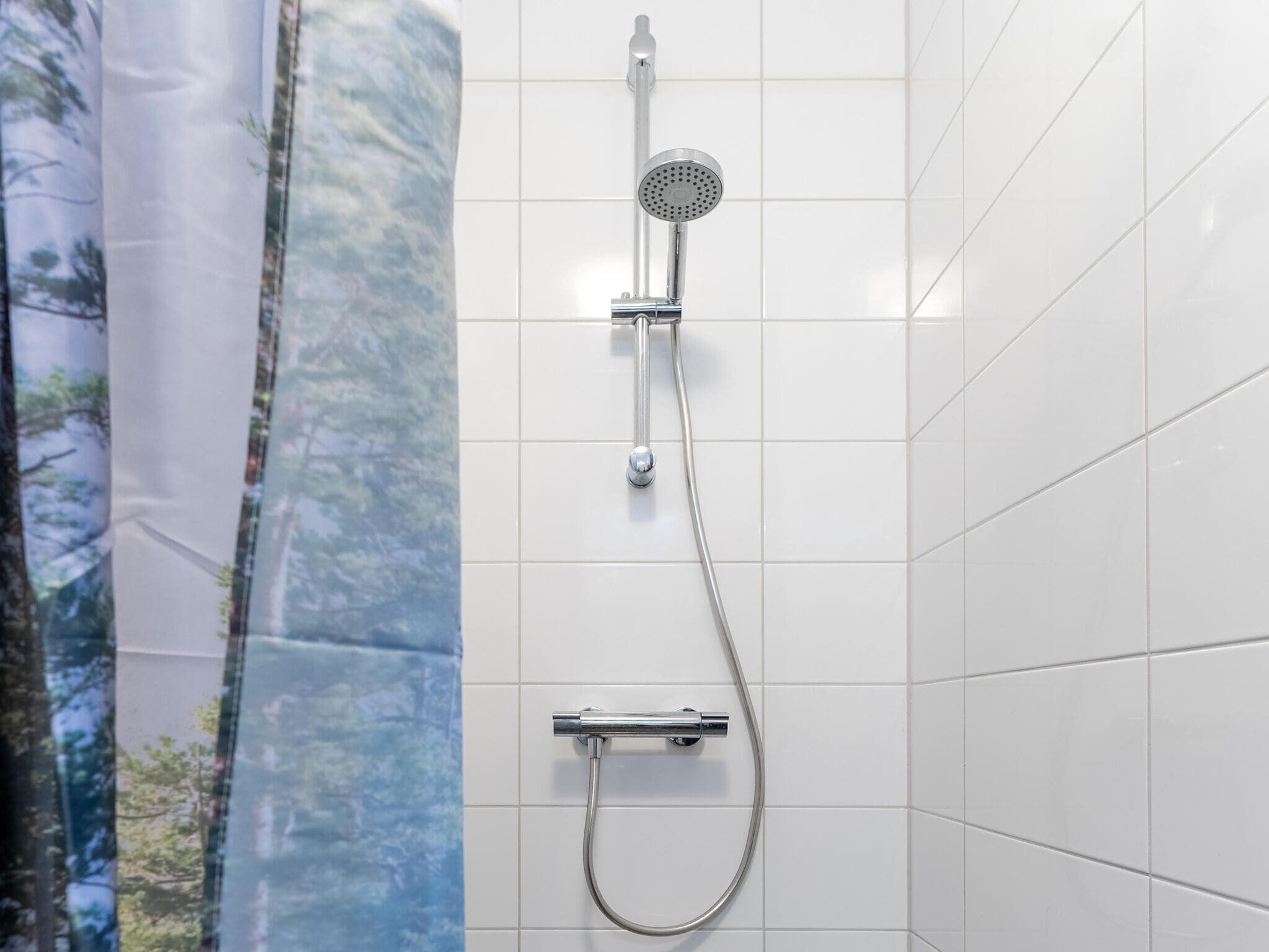 Una ducha con cabezal de ducha de mano y manguera, fijada en una pared de azulejos.