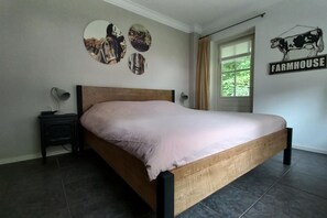 A bedroom with a wooden bed, a nightstand, a lamp, and wall art including a cow illustration and circular pictures. - Cosy holiday home with a private garden (Winterswijk Meddo)