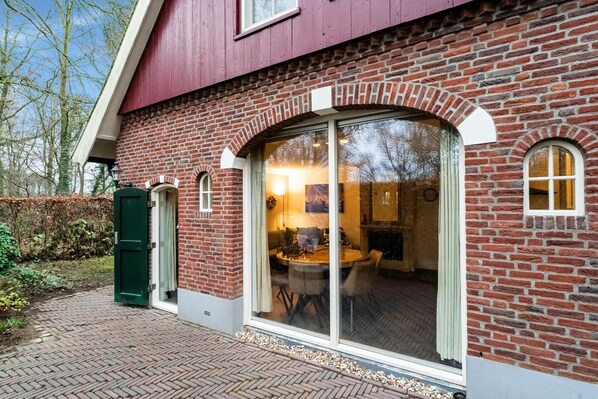 A brick house with large glass doors leading to a dining area. - Cosy holiday home with a private garden (Winterswijk Meddo)