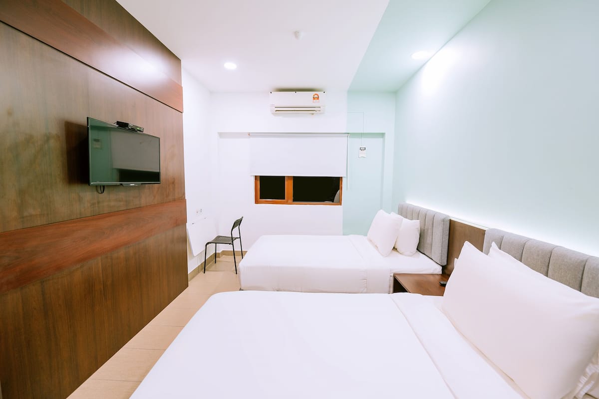 Ein Hotelzimmer mit zwei Betten, einem an der Wand befestigten Fernseher, einer Klimaanlage, einem Fenster und einem Sessel.