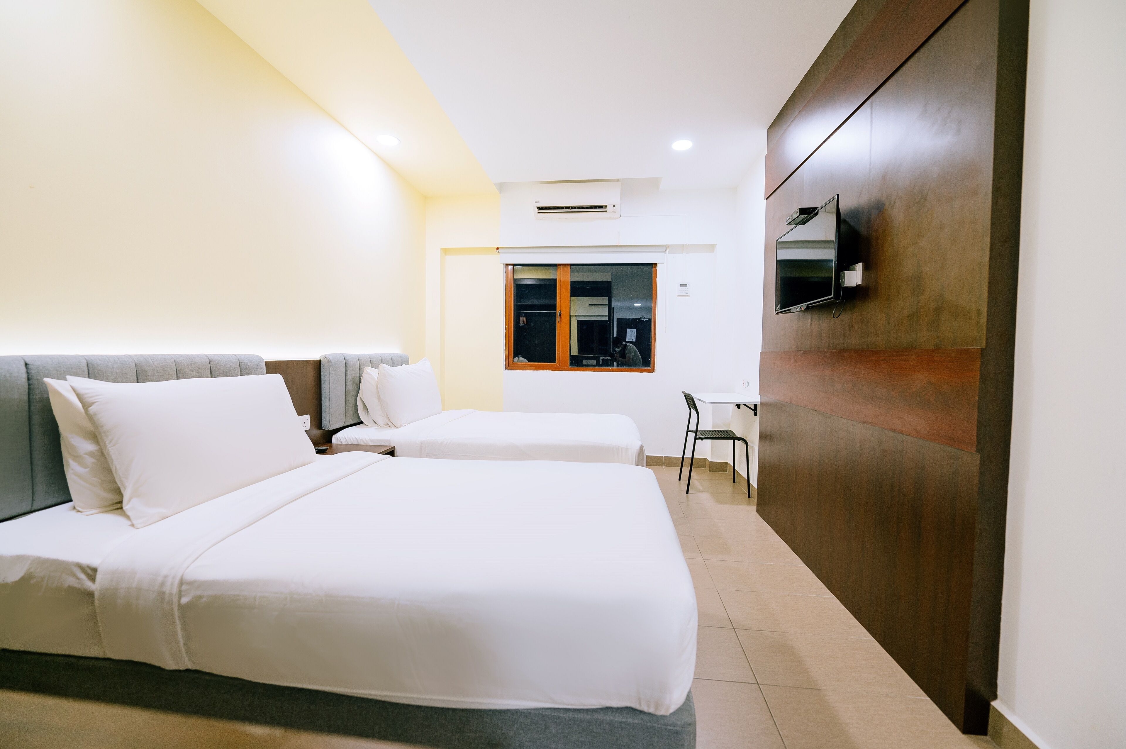 A hotel room with two beds, a desk, a chair, and a TV mounted on the wall.