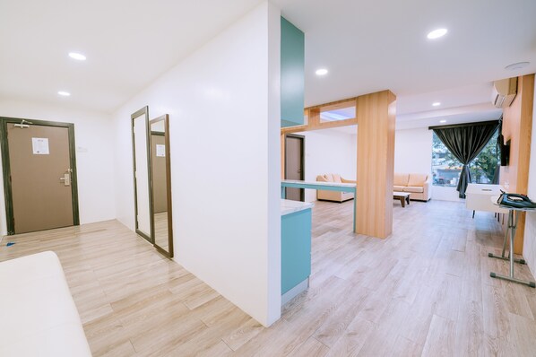 A modern hotel room with a wooden floor, a bed, a desk, and a window with curtains.