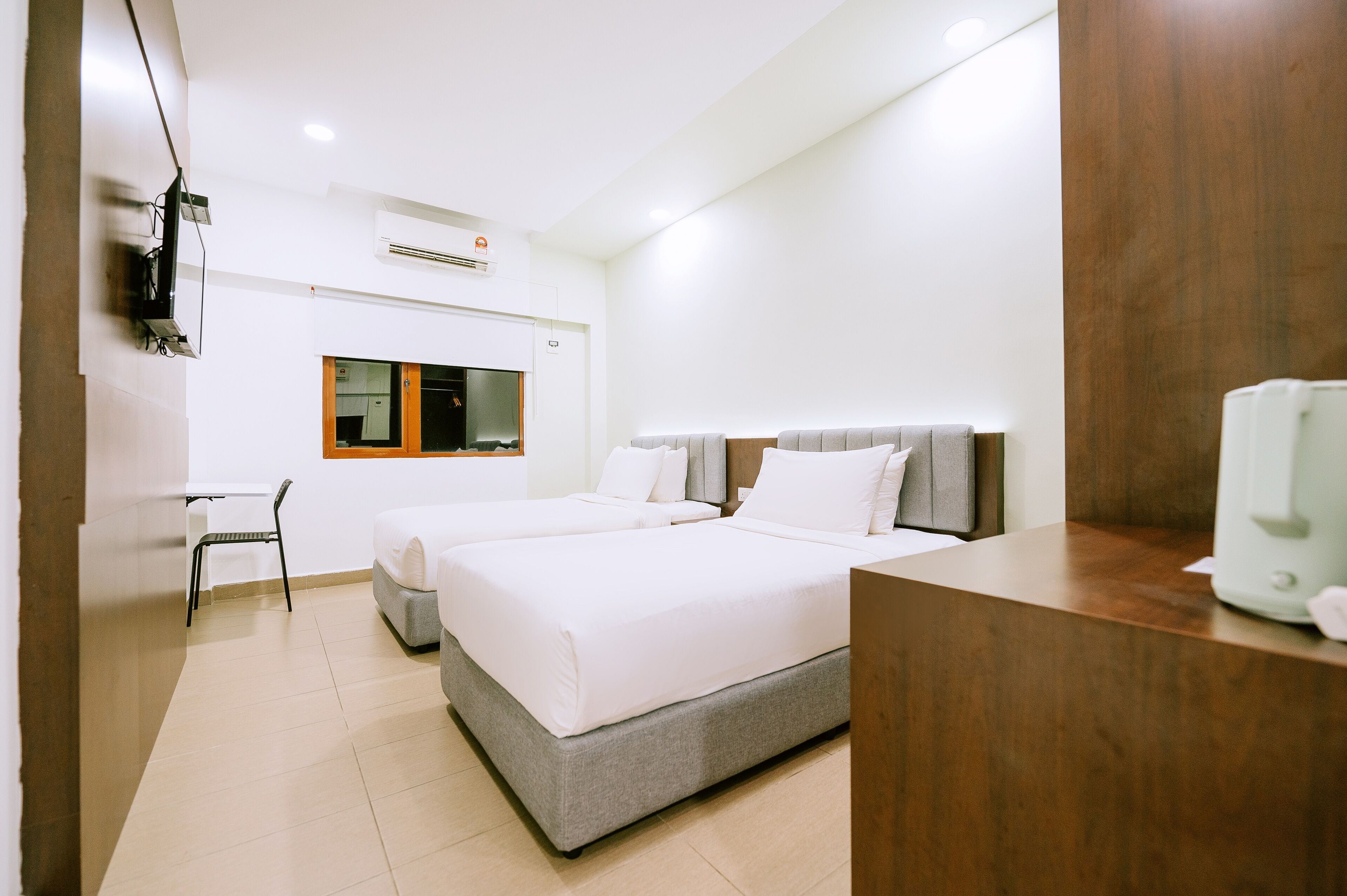 A modern hotel room with two beds, a desk, a chair, and a coffee maker.