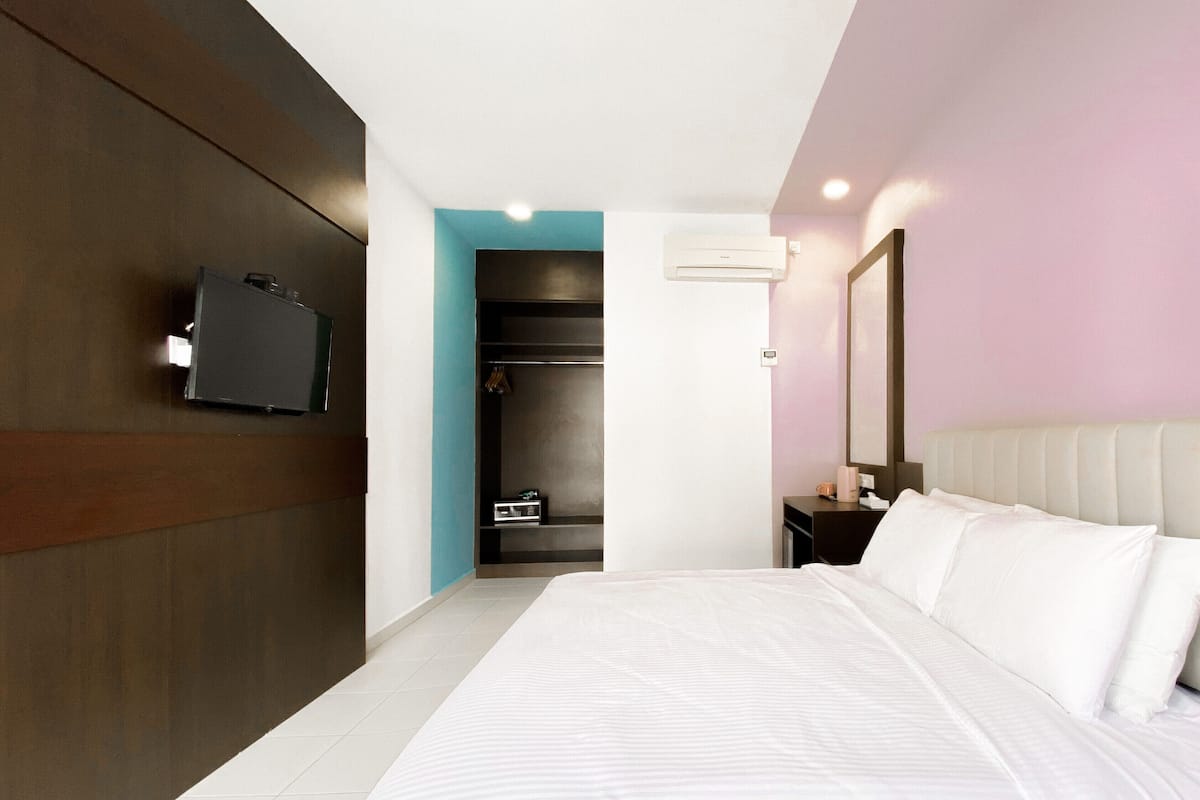 Ein modernes Hotelzimmer mit einem großen Bett, einem an der Wand montierten Fernseher, einem begehbaren Kleiderschrank und einer Klimaanlage.