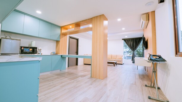 A modern kitchen with teal cabinets, a microwave, and a coffee machine. There is a wooden bench and an ironing board in the living area. - The Concept Hotel Langkawi (Langkawi)