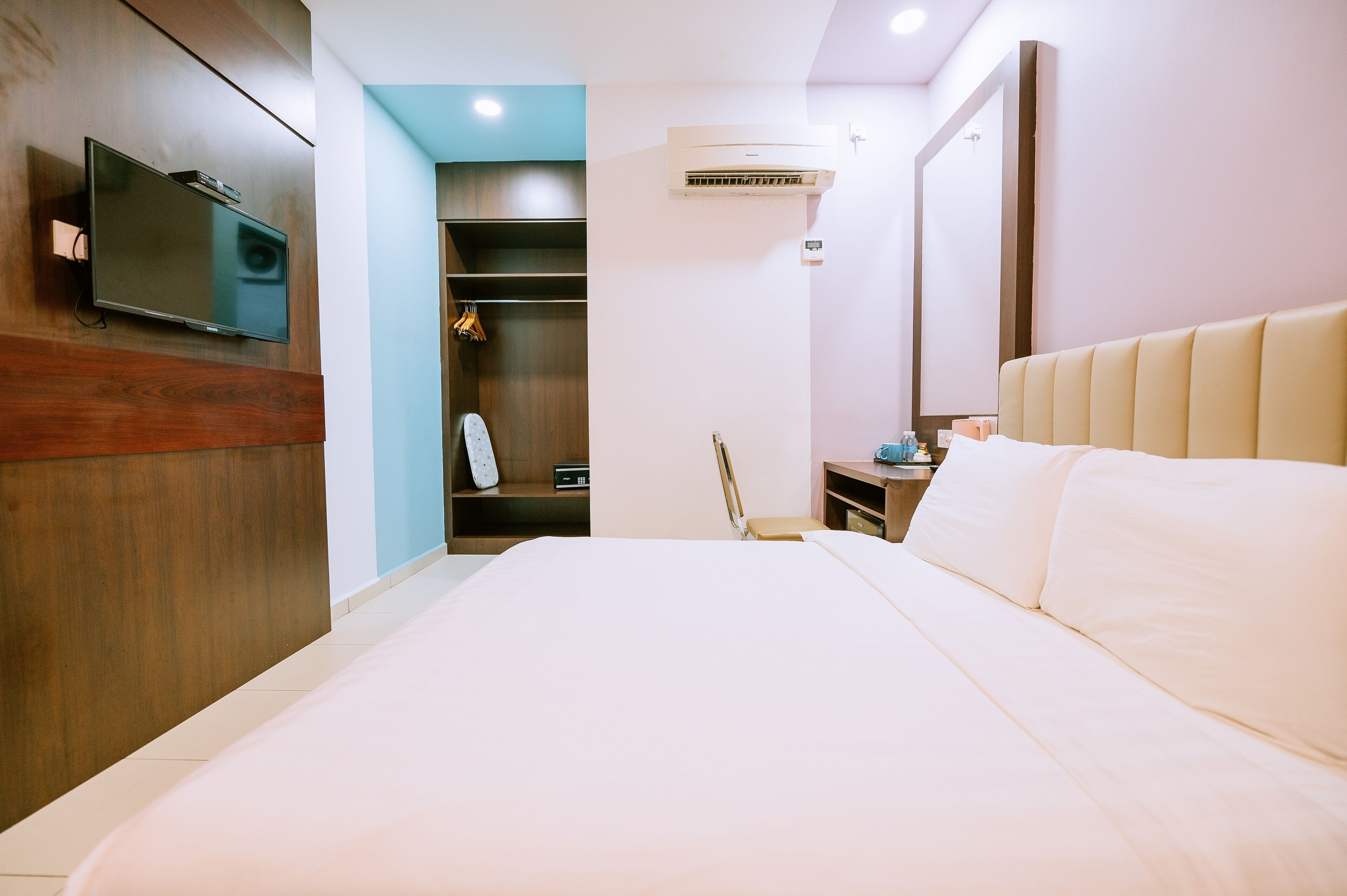 A hotel room with a large bed, a flat-screen TV mounted on the wall, a wardrobe, and a small desk with a chair.