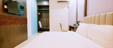 A hotel room with a large bed, a flat-screen TV mounted on the wall, a wardrobe, and a small desk with a chair.