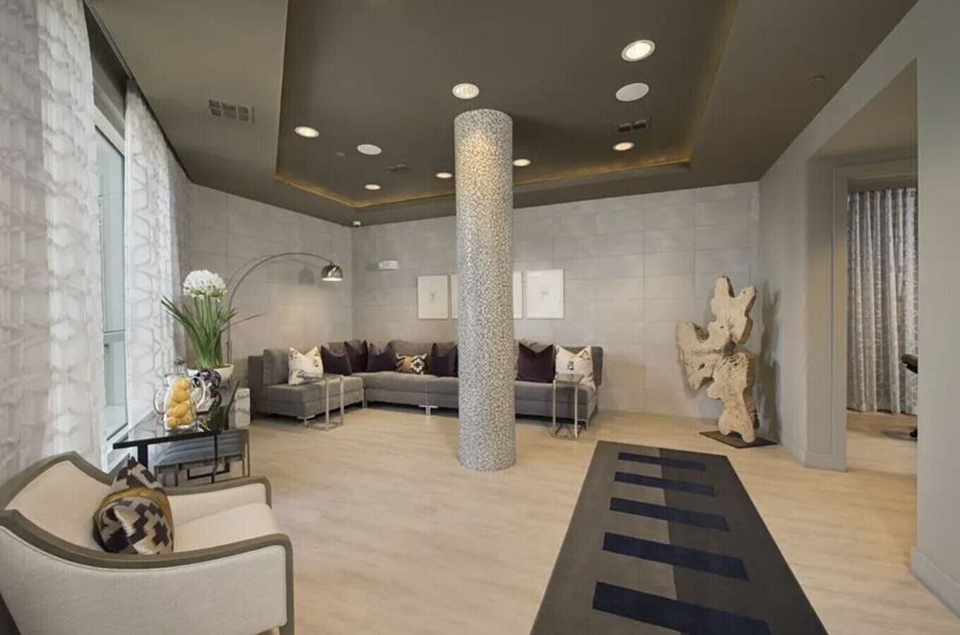 Um lobby moderno com um grande pilar central, sofás, uma mesa de centro e uma escultura de parede única.
