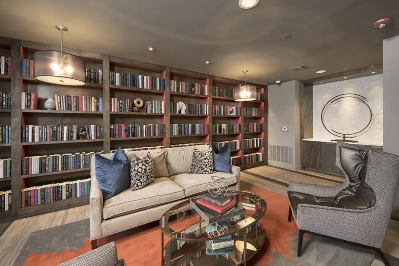 Een moderne woonkamer met een bank, salontafel en fauteuil, omringd door boekenplanken vol boeken.