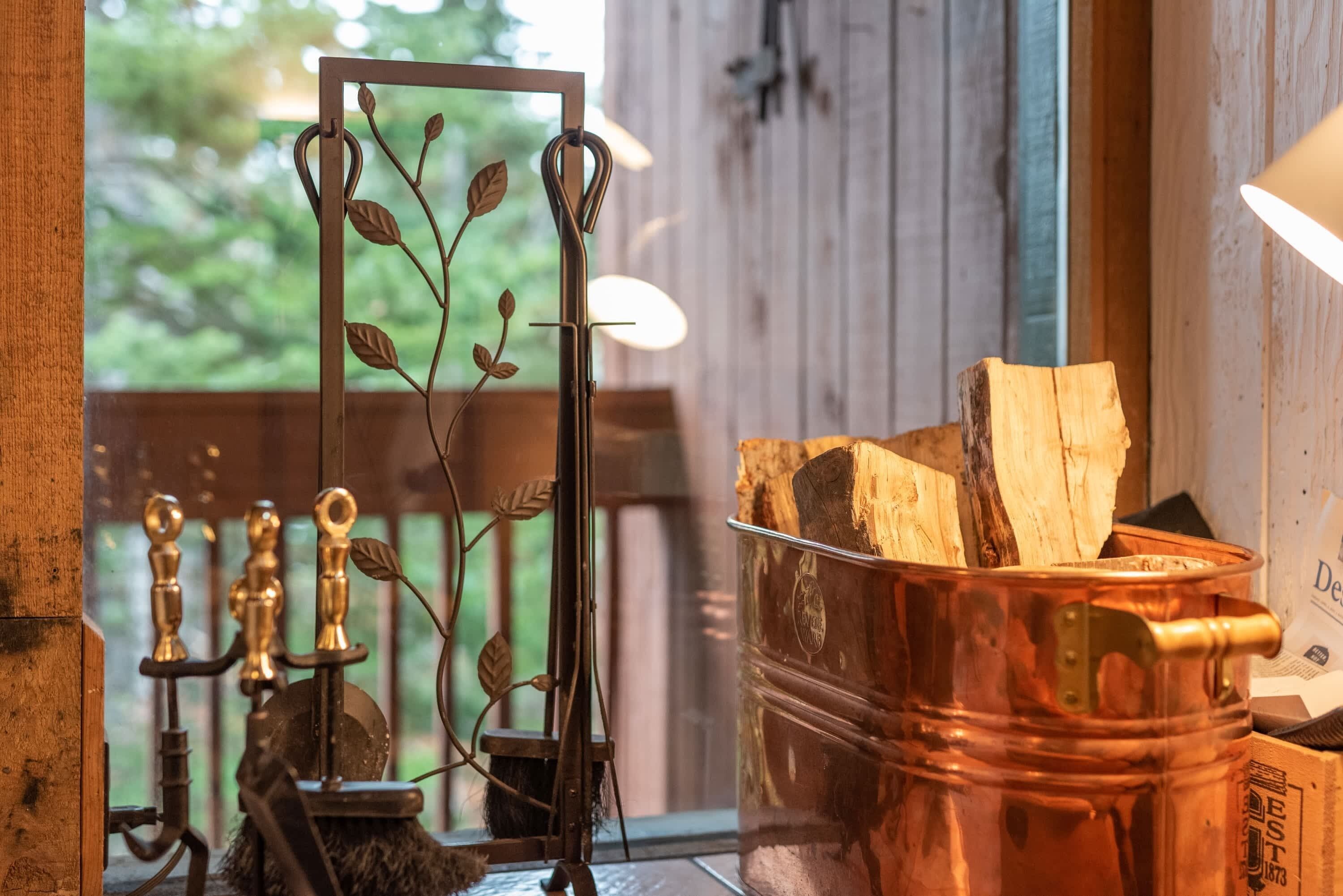 Een rustiek interieur met een bladdecoratie van metaal, een houten bank en een koperen pot gevuld met houtblokken.