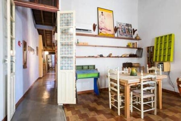 Un couloir étroit doté d’un plancher en bois, une table à manger avec des chaises et des étagères remplies de divers objets.