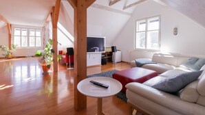 A spacious living room with a high ceiling, wooden beams, a flat-screen TV, a sofa, and a coffee table. - Apartment in the heart of Bled with views (Bled)