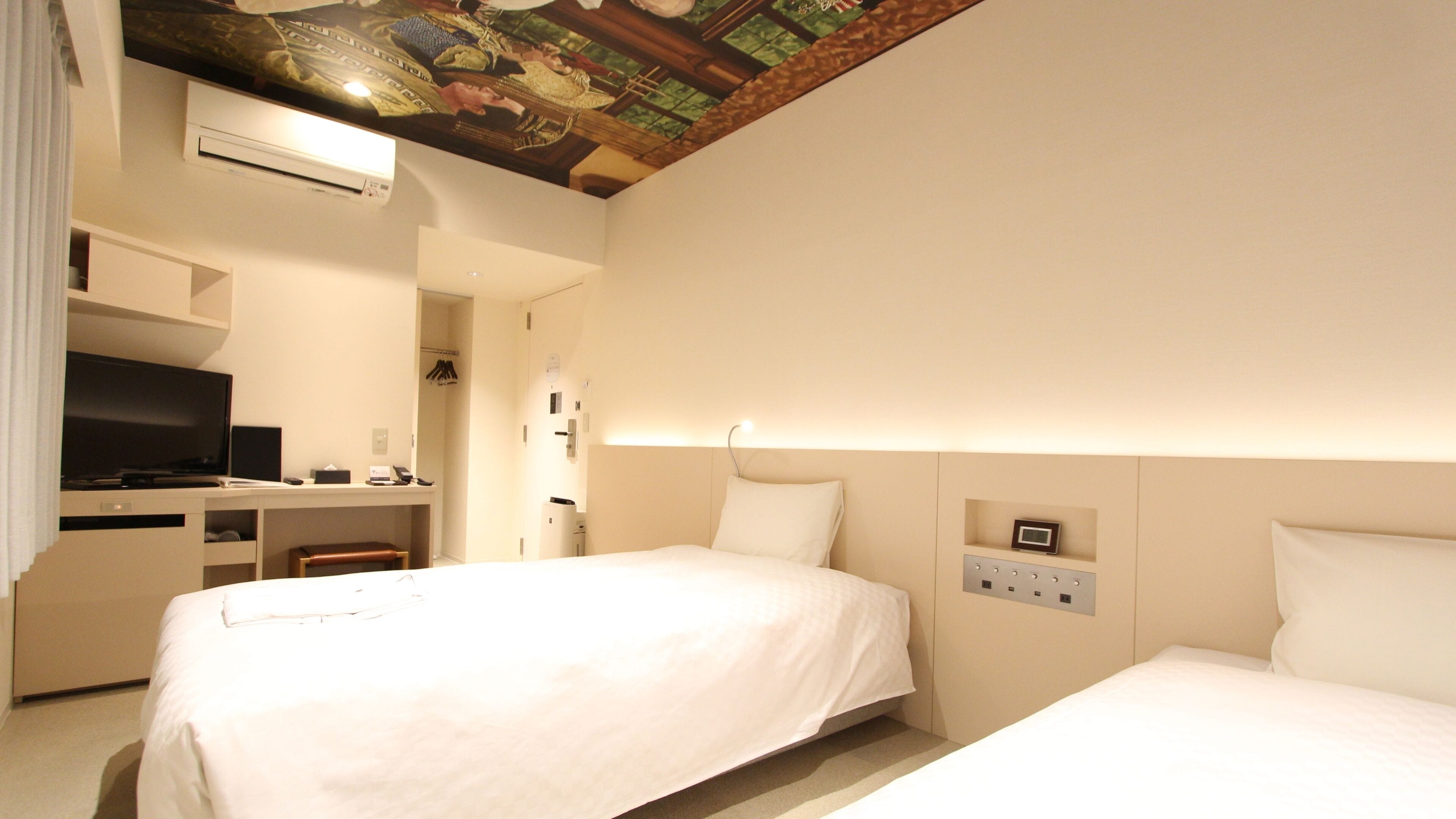 A hotel room with two beds, a desk with a TV, and a ceiling with a decorative design.