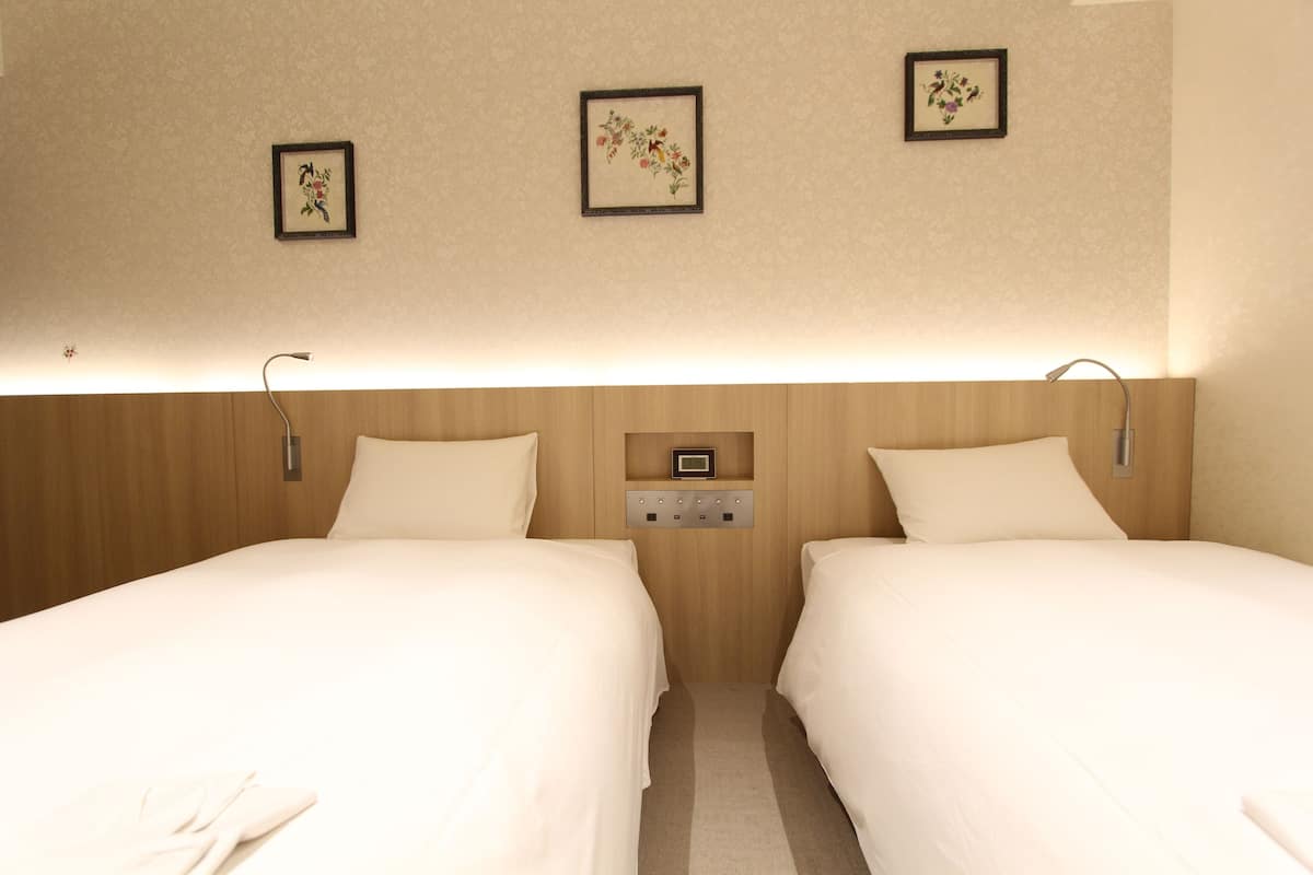 Habitación de hotel con dos camas, cabecera de madera, un reloj en la pared y cuadros con motivos florales.