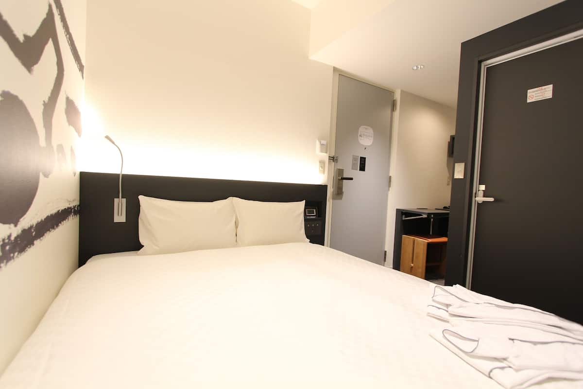 Habitación de hotel con una cama grande, una mesita de noche, una lámpara de pared y acceso a un baño.