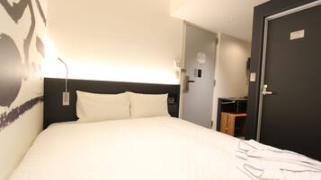 Quarto de hotel com cama grande, mesa de cabeceira, luminária na parede e porta para o banheiro.