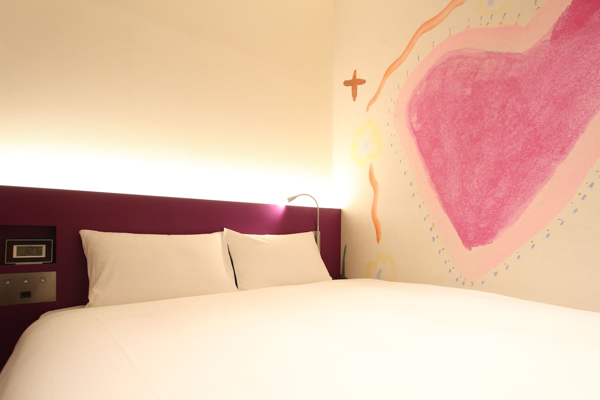 Una cama con ropa de cama blanca, un cabecero morado y una pared con un diseño de gran corazón.