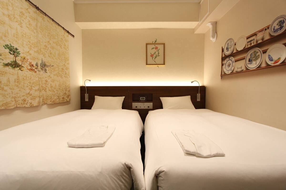 Una cama doble con ropa blanca y un cabecero con panel de control.