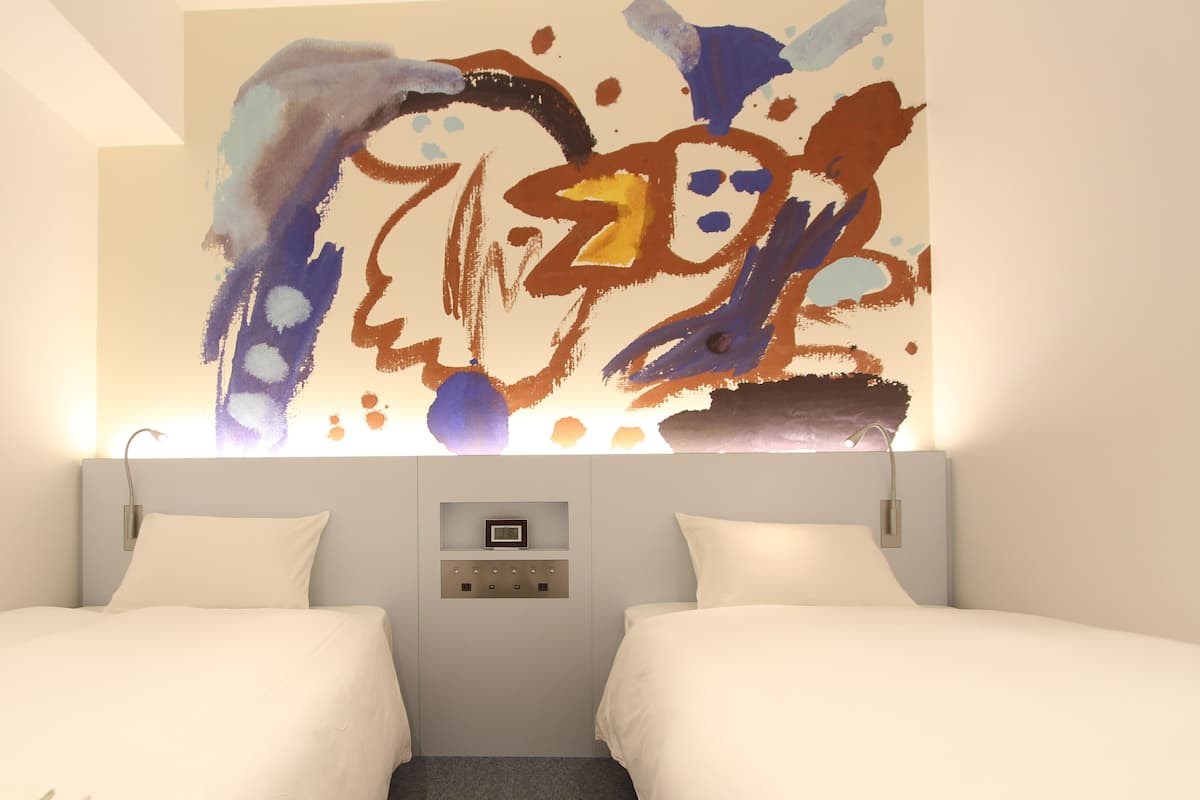 Habitación de hotel con dos camas, una obra de arte en la pared, un panel de control y una lámpara en el techo.