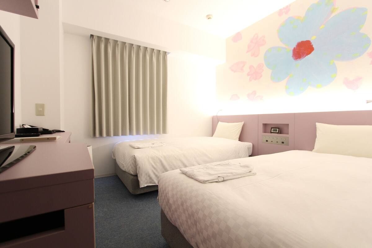 Una habitación de hotel con dos camas, un escritorio y un televisor montado en la pared.
