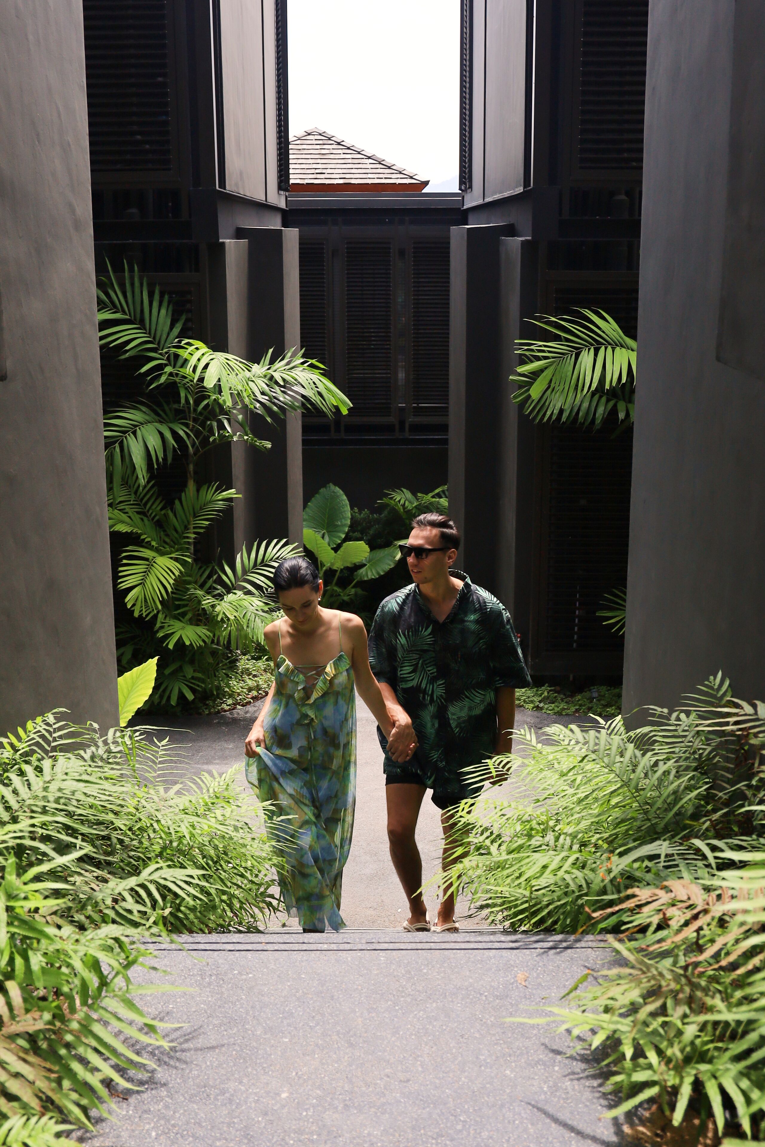 A couple walking through a modern building with a pathway surrounded by lush greenery.