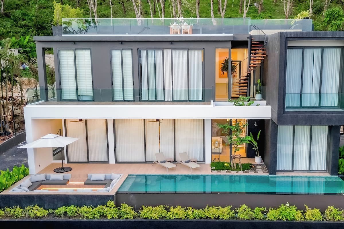 A modern two-story house with a swimming pool, large windows, and outdoor seating.