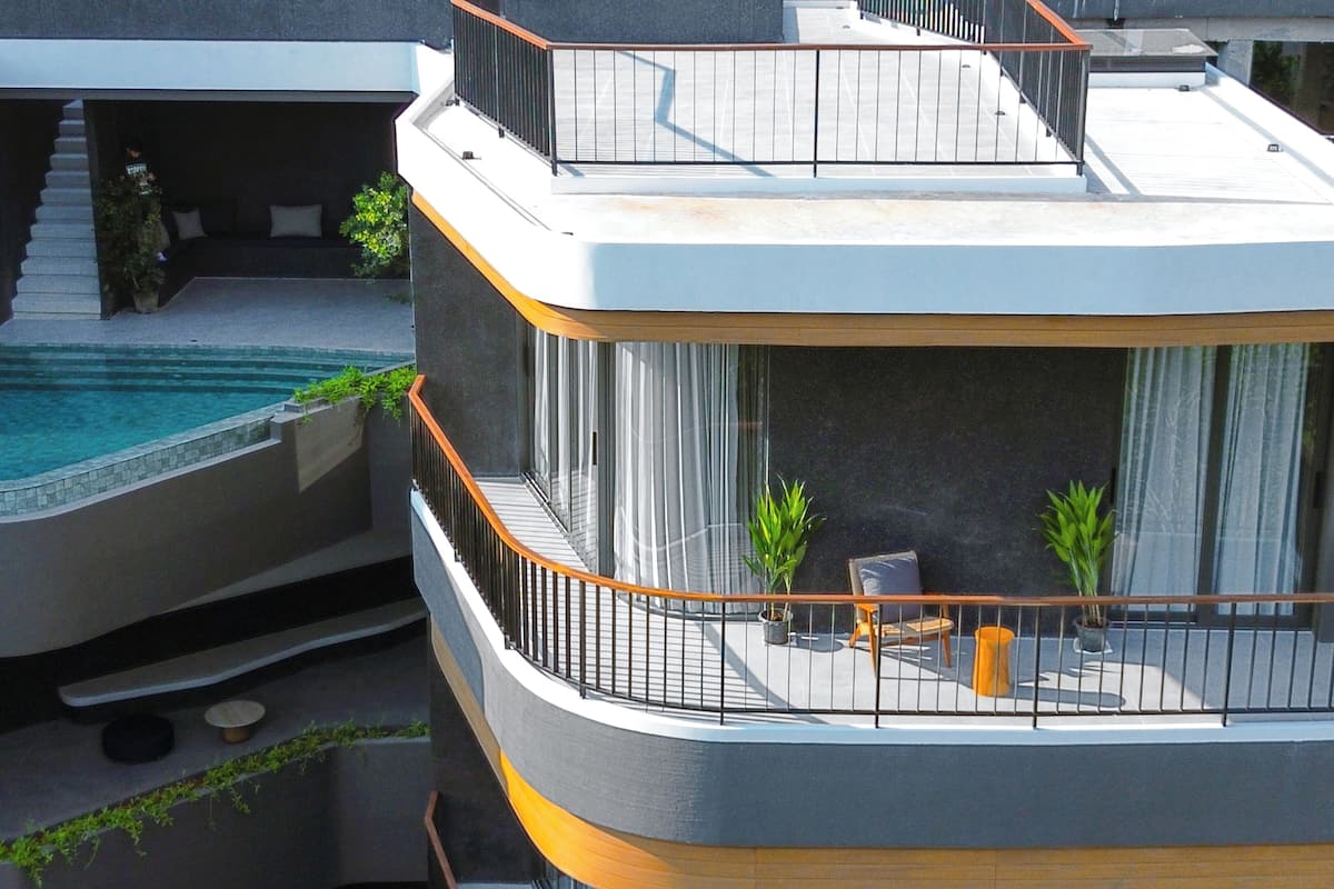 A modern multi-level residential building with a rooftop pool, outdoor seating, and a staircase leading to an upper level.