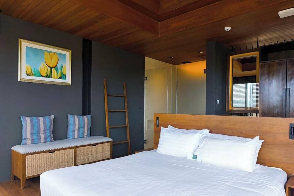 A bedroom with a large bed, a bench with pillows, a ladder, and a painting on the wall.