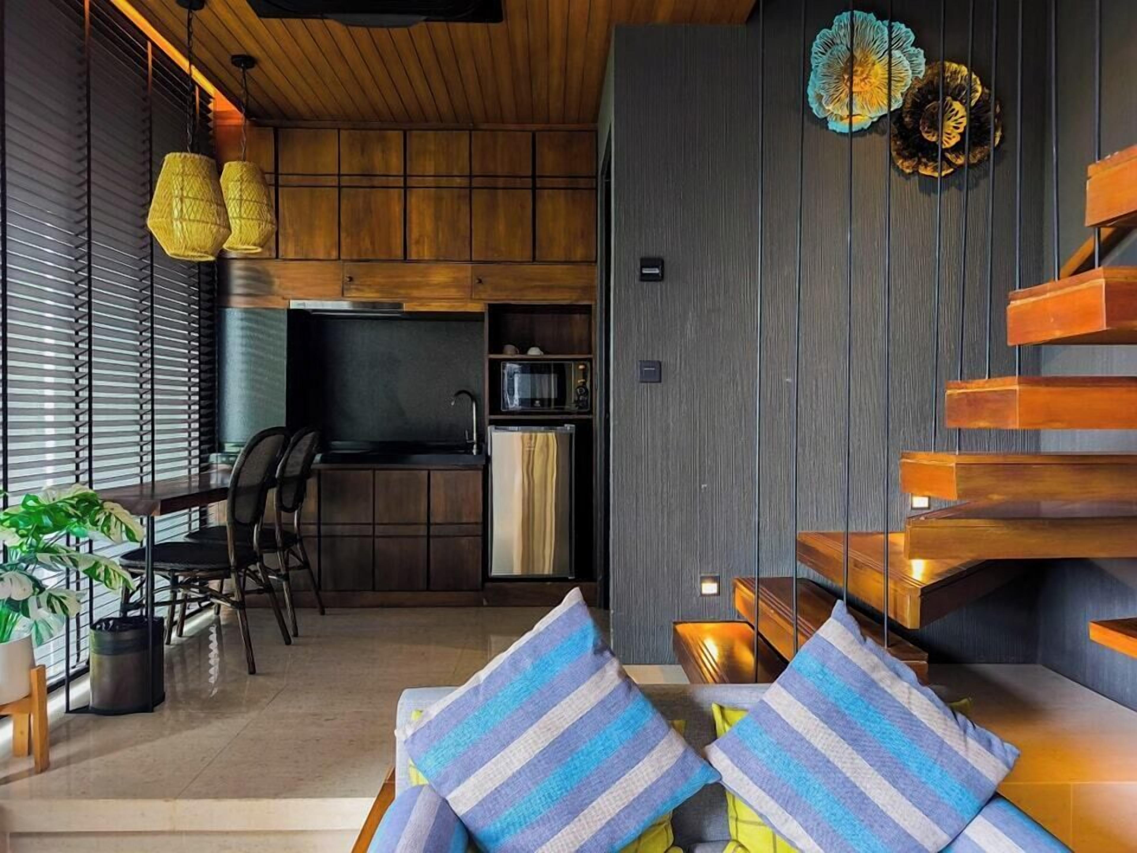A modern kitchen with wooden cabinets, a built-in microwave, and a sink. There is a dining area with chairs and a table, and a staircase with wooden steps.