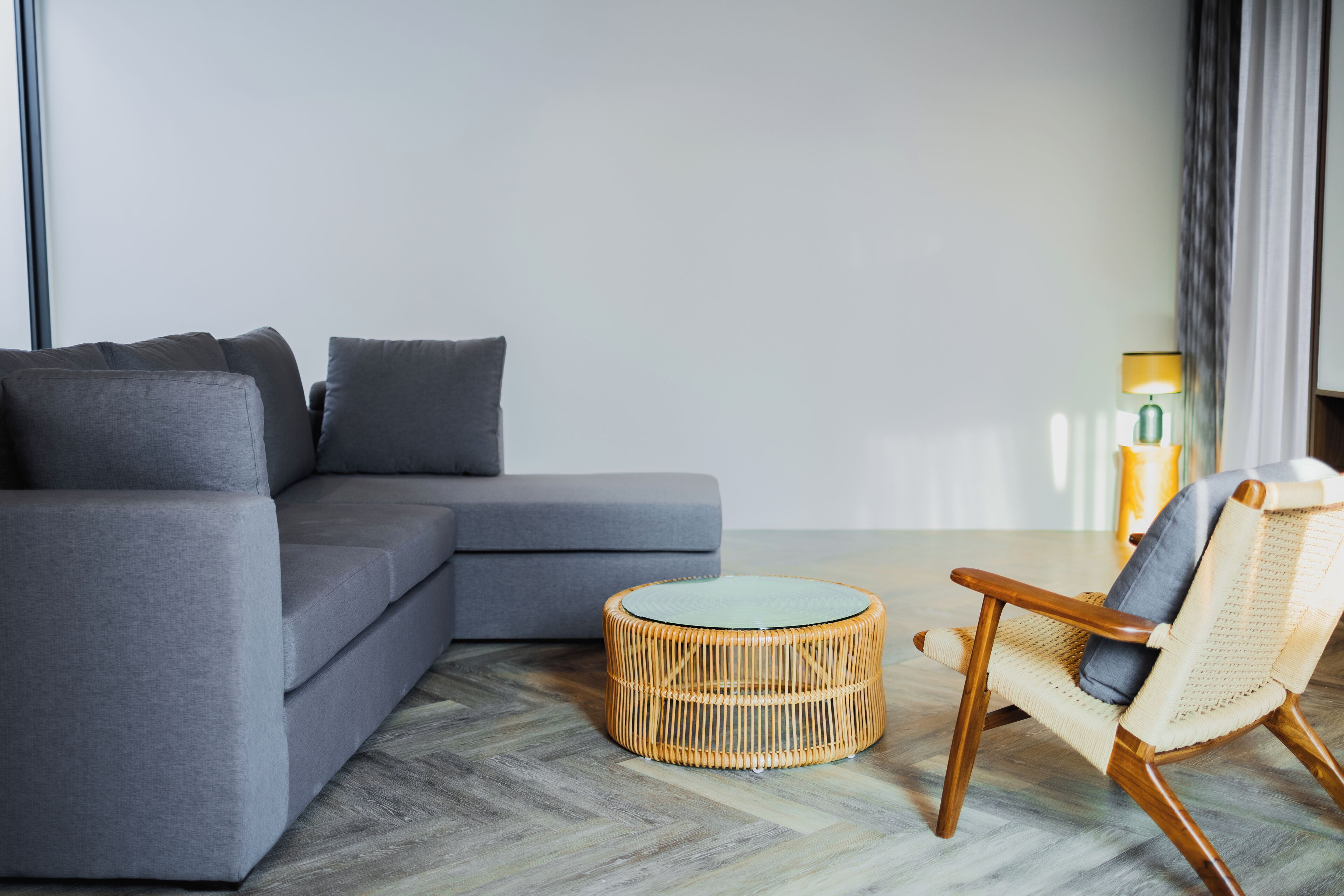 Ein modernes Wohnzimmer mit einem grauen Ecksofa, einem runden Korbstuhl und einem kleinen runden Tisch.