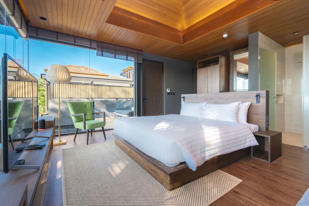 A modern bedroom with a large bed, a desk, and a chair, with a view of the outside.