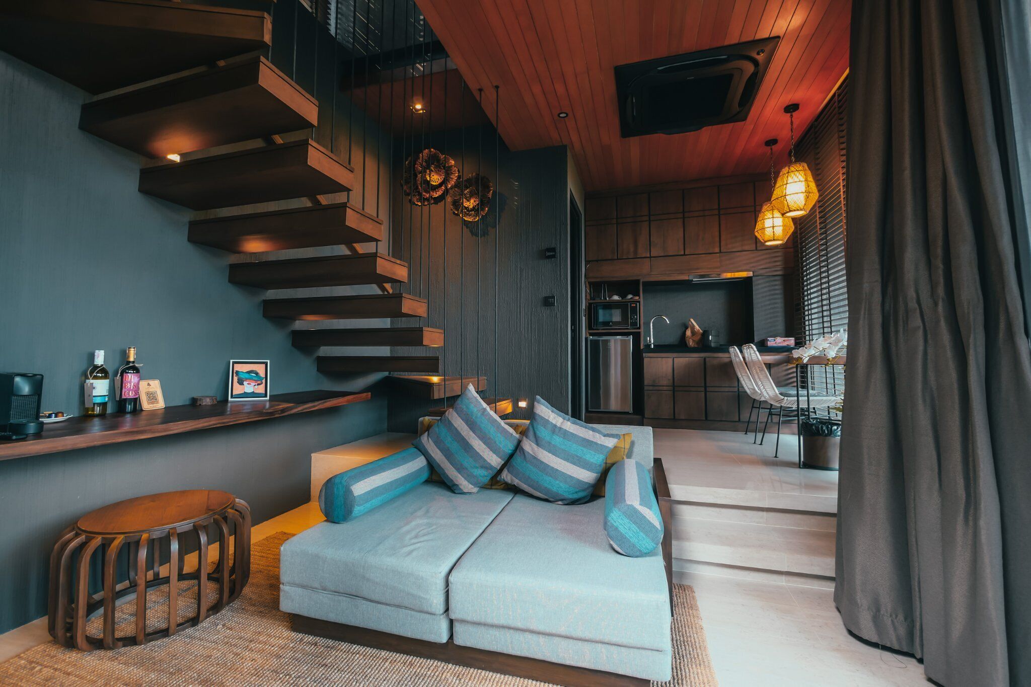 Una sala de estar moderna con un sofá, una escalera de madera, una zona de cocina y un comedor.