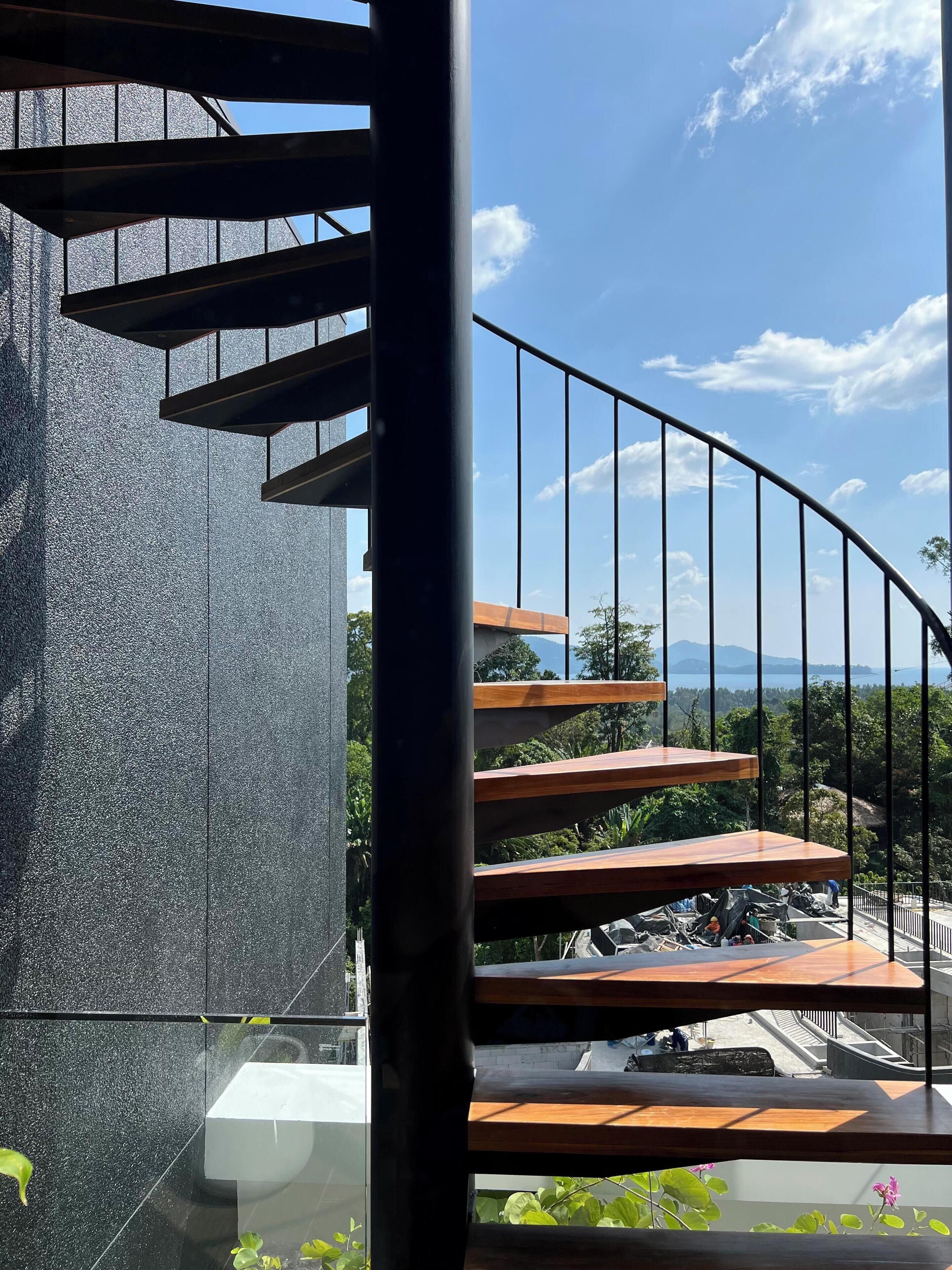 A spiral staircase with a view of a parking area and greenery below.