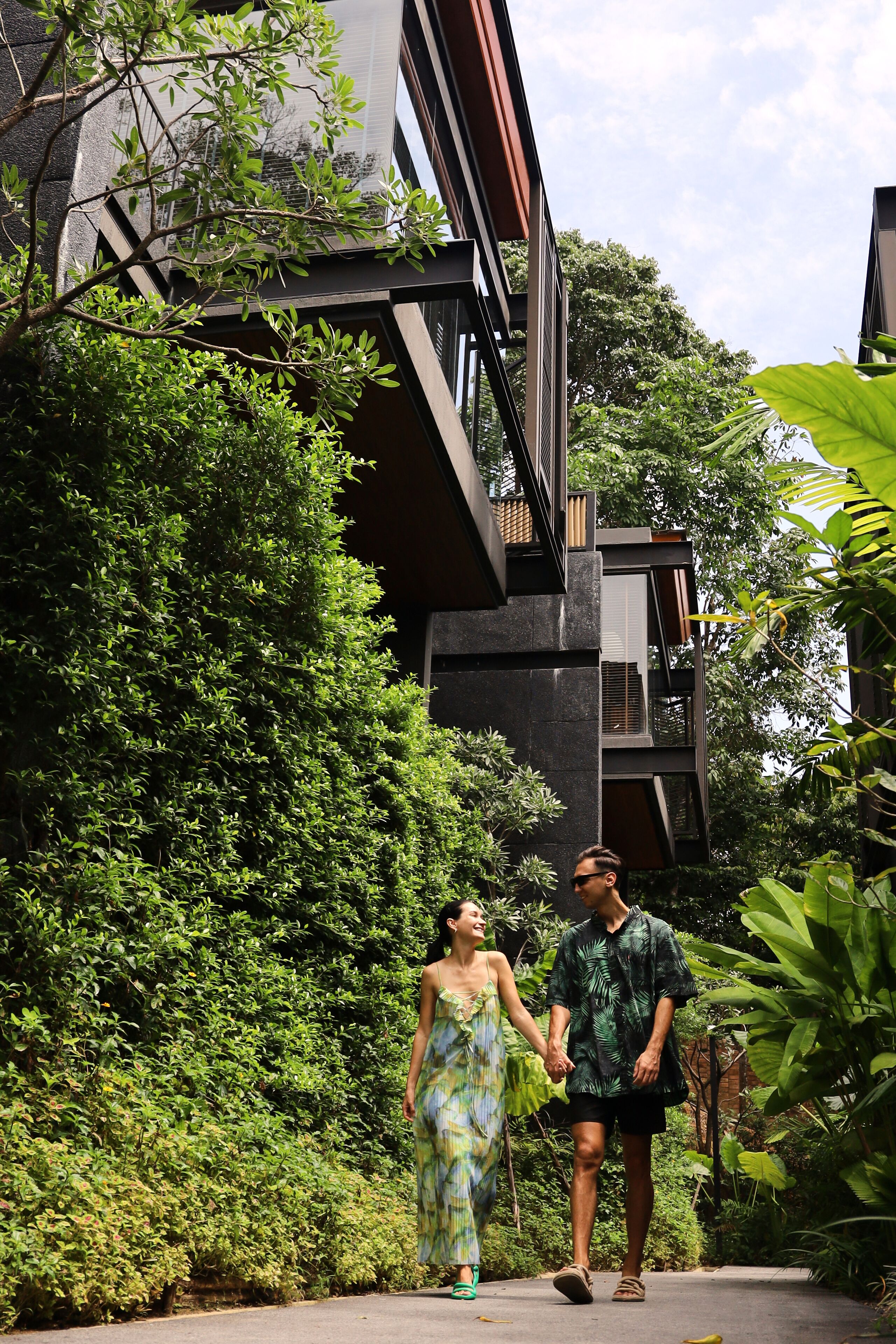 A couple walking on a pathway surrounded by lush greenery and modern architecture.