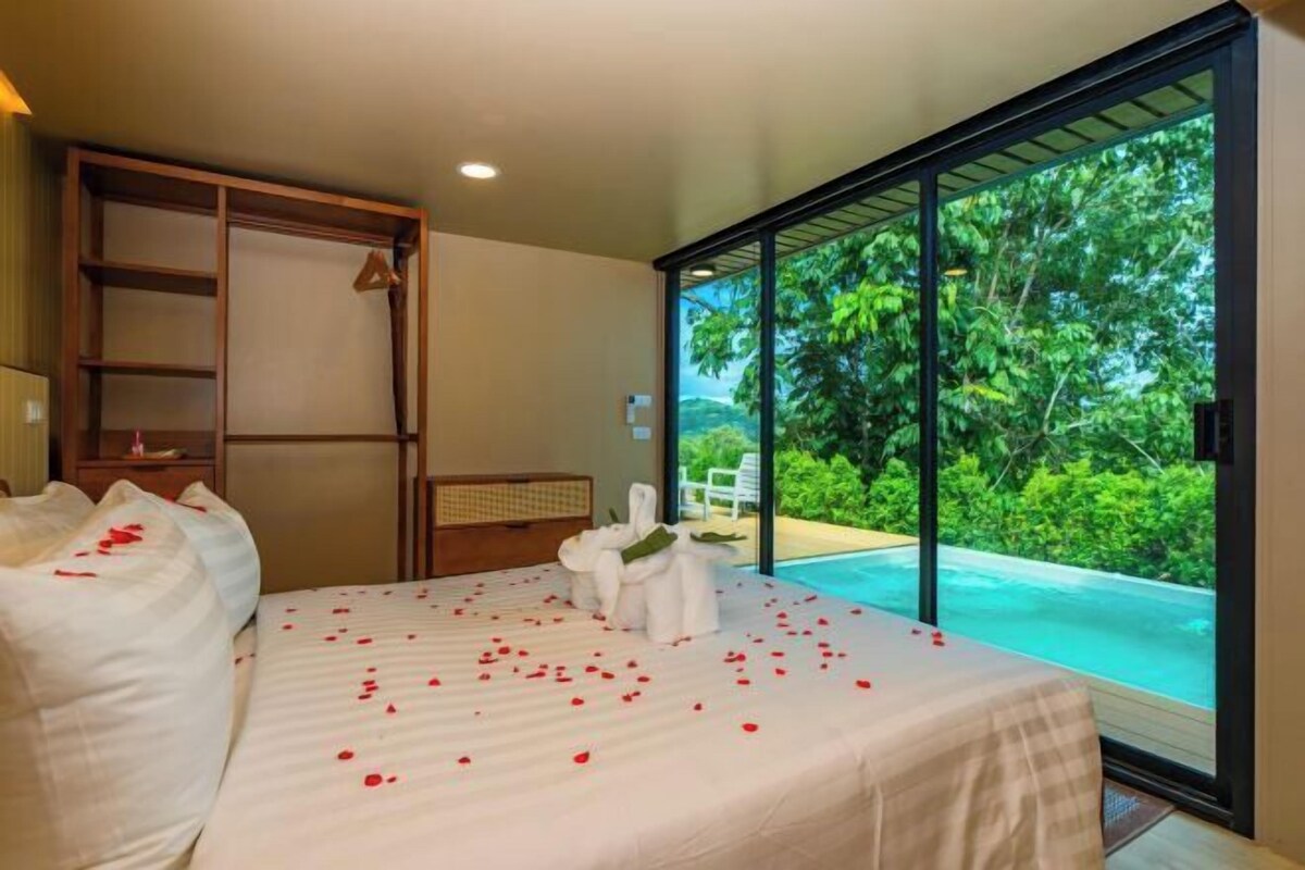 A bedroom with a bed, a wooden wardrobe, and a view of a swimming pool.