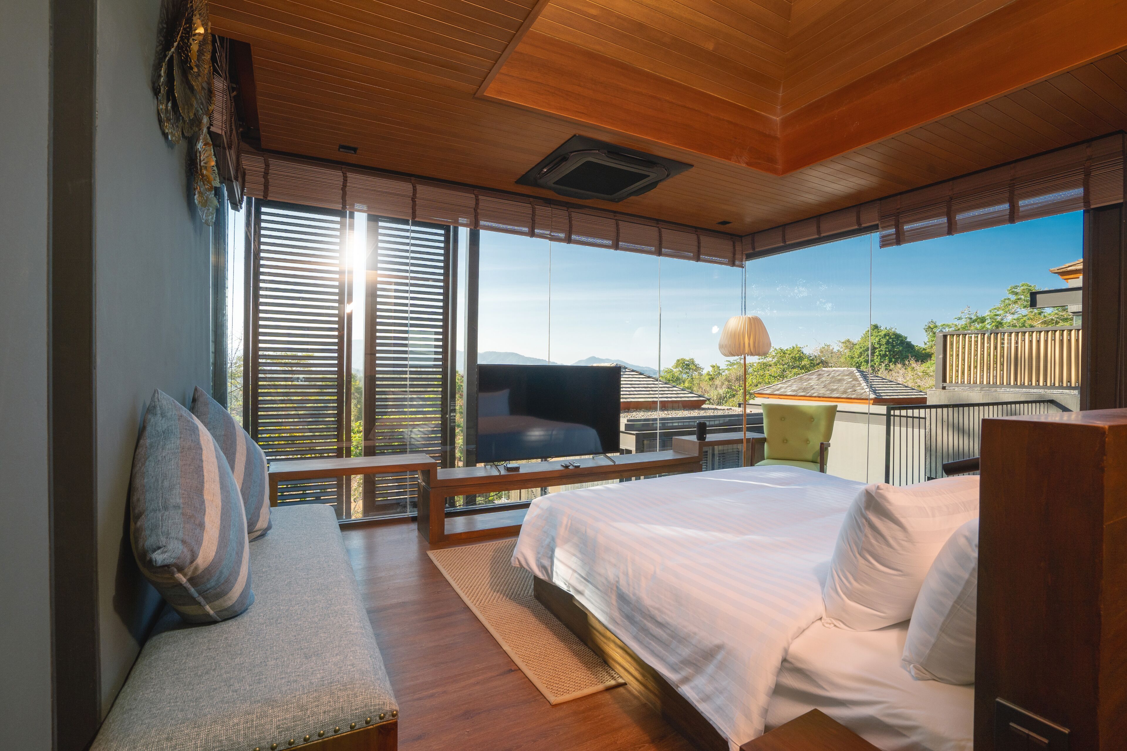 A modern bedroom with a large bed, a flat-screen TV, and a view of the outdoors.