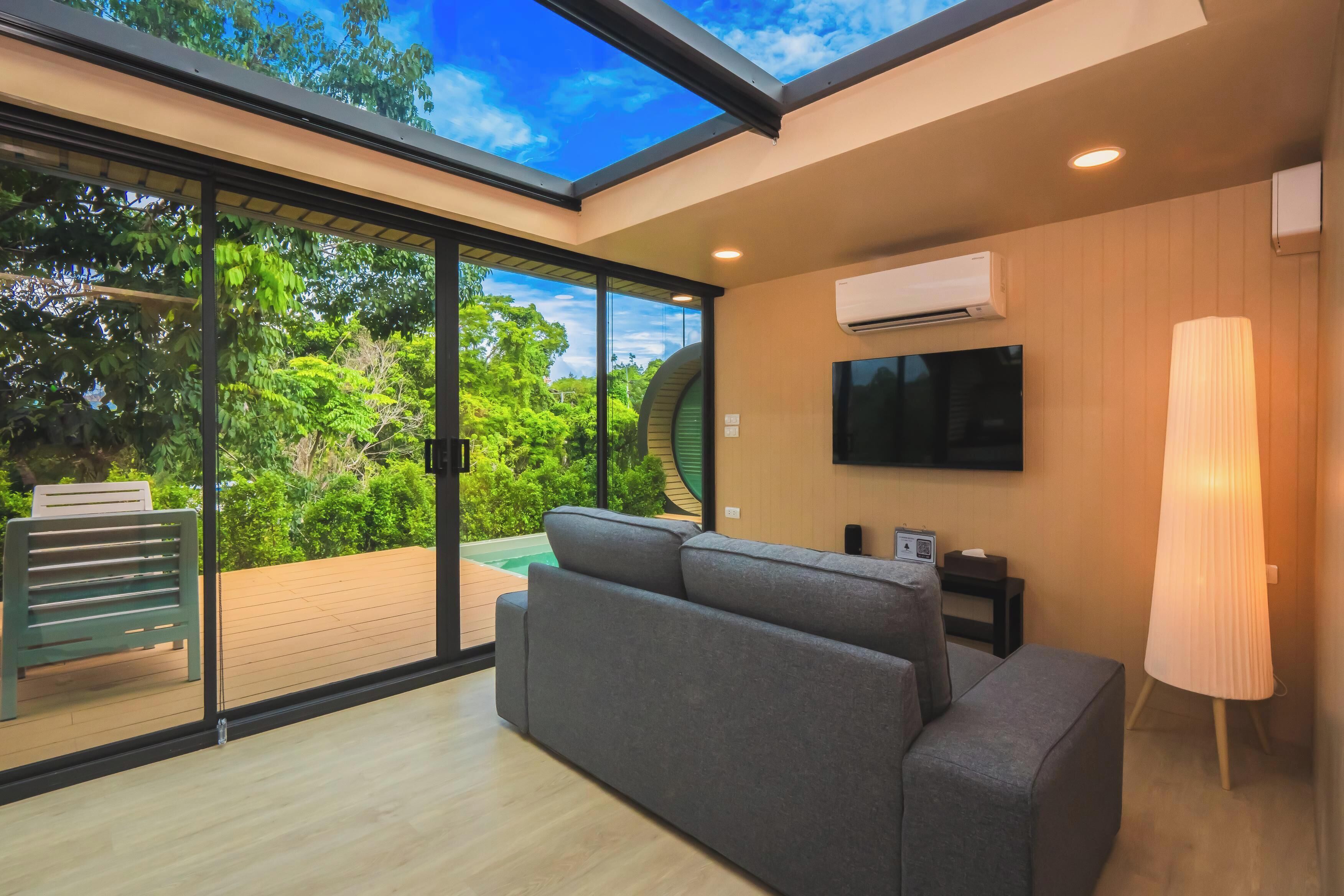A modern living room with a large glass door leading to a balcony, a flat-screen TV mounted on the wall, and a floor lamp.
