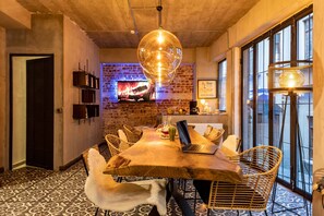 A dining area with a wooden table, wicker chairs, a laptop, and a television displaying a fire. - Green Parrot Hotel (Istanbul)