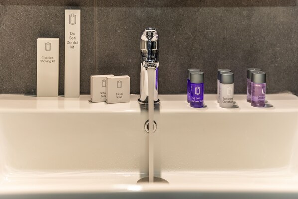 Un lavamanos de baño con un grifo moderno, un kit de higiene bucal y diversos productos de cuidado personal.