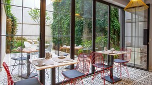 A modern outdoor café with tables and chairs, large windows, and greenery visible through the glass. - Green Parrot Hotel (Istanbul)