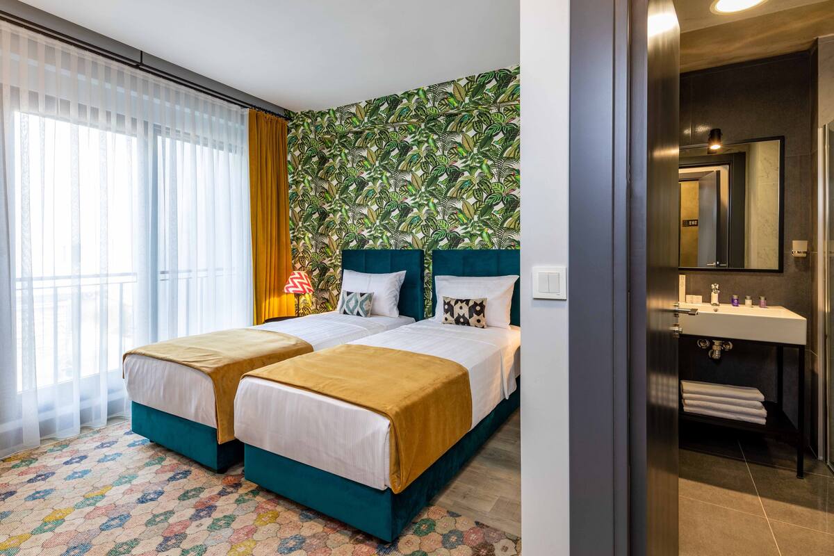 A hotel room with two beds, a bathroom with a sink, and a patterned wall.