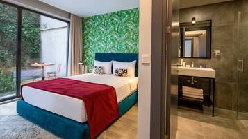 Habitación de hotel moderna con una cama grande, un baño con espejo y lavamanos, y vistas al verdor exterior.