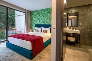 A modern hotel room with a large bed, a bathroom with a mirror and sink, and a view of greenery outside. - Green Parrot Hotel (Istanbul)