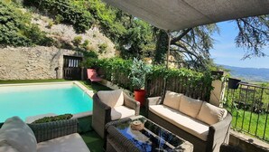 A poolside area with wicker furniture, a glass table, and a view of a mountainous landscape. - Panoramic view Quiet private pool (Rasteau)
